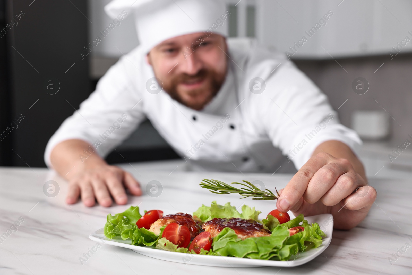 Photo of Professional chef decorating delicious dish with rosemary at white marble table in kitchen, selective focus