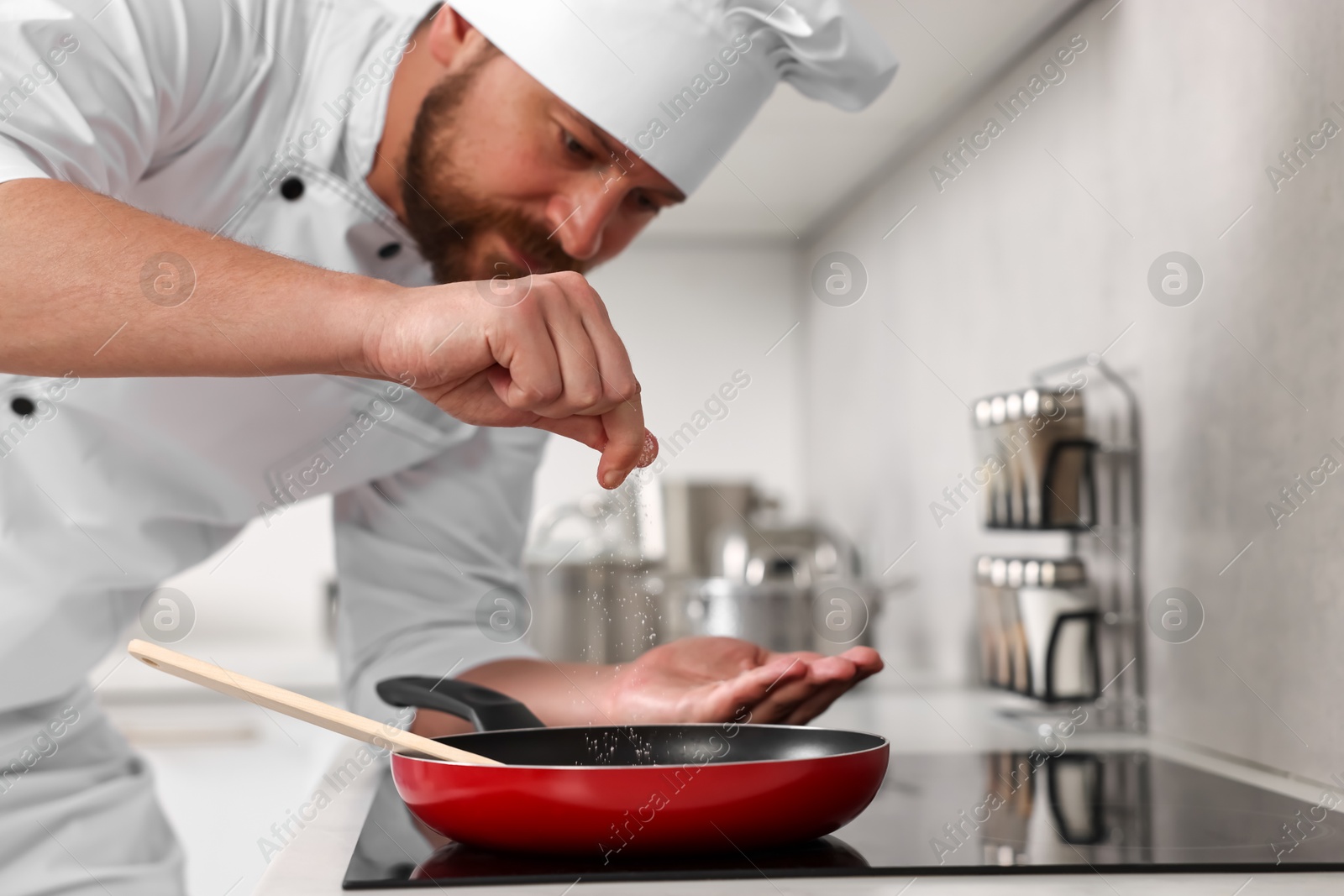 Photo of Professional chef adding salt into frying pan in kitchen