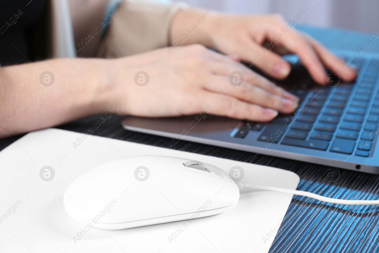 Photo of Woman working with laptop at black wooden table, focus on computer mouse