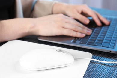 Photo of Woman working with laptop at black wooden table, focus on computer mouse