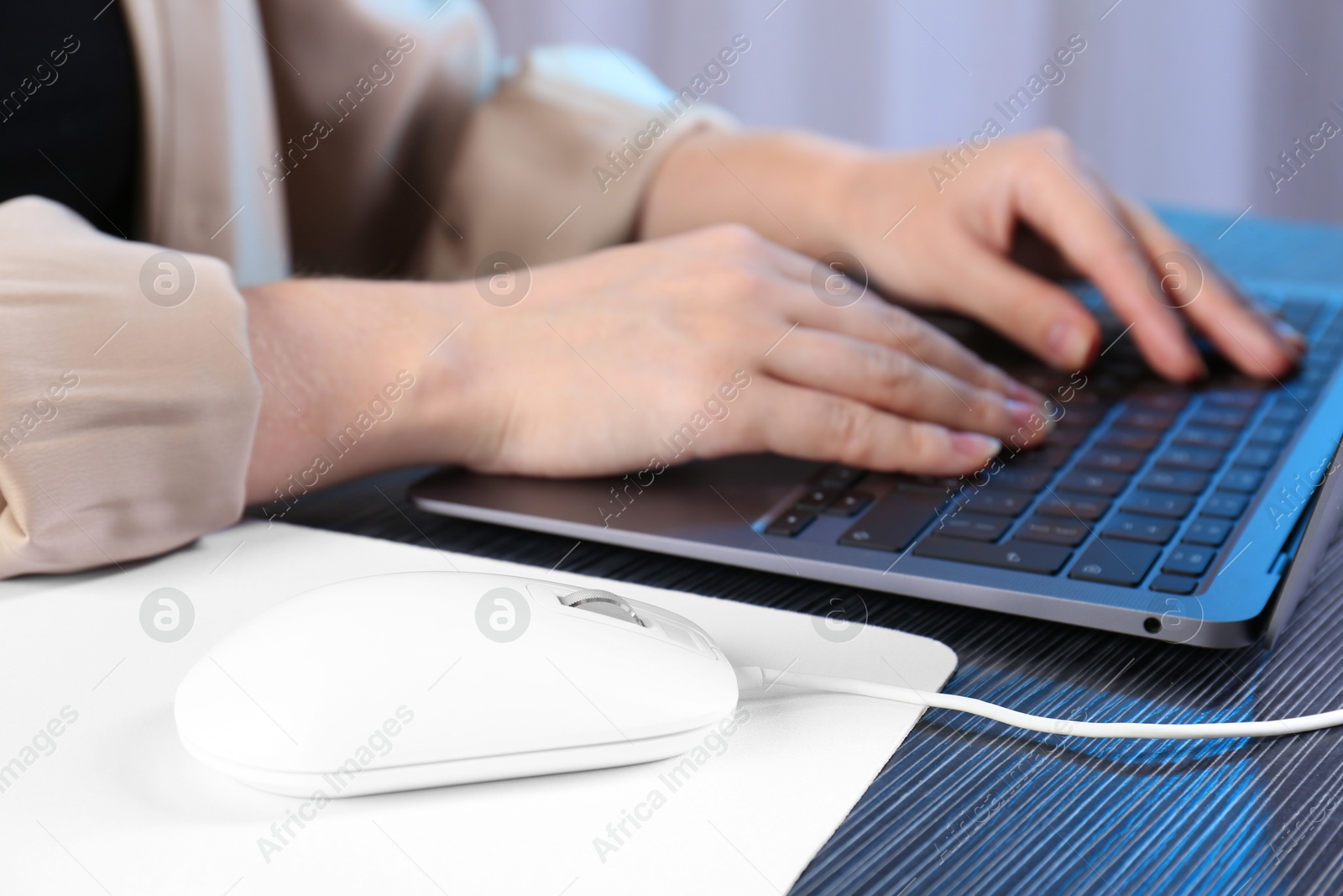 Photo of Woman working with laptop at black wooden table, focus on computer mouse