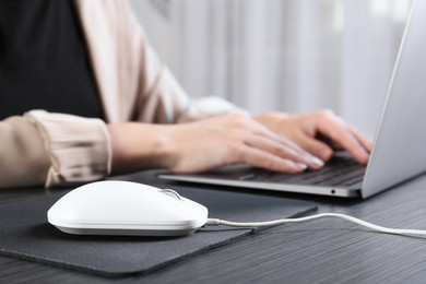 Photo of Woman working with laptop at black wooden table, focus on computer mouse