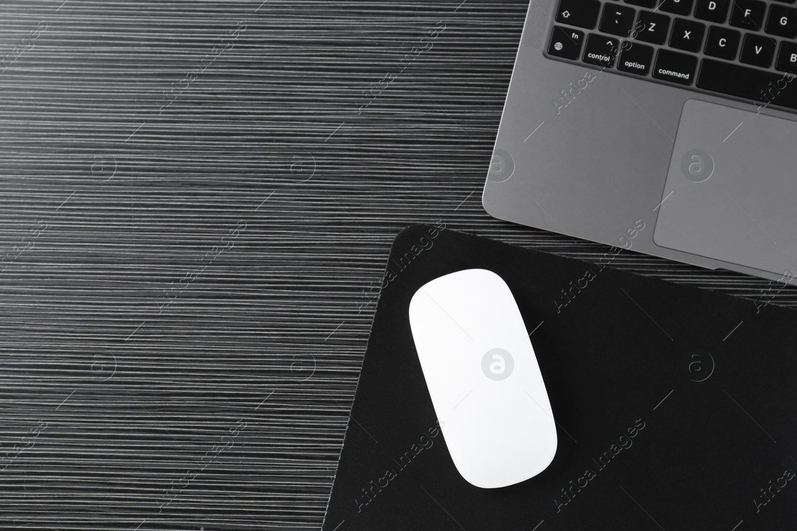 Photo of White computer mouse with mousepad and laptop on black wooden table, flat lay