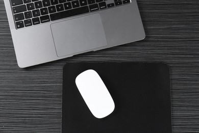 Photo of White computer mouse with mousepad and laptop on black wooden table, flat lay