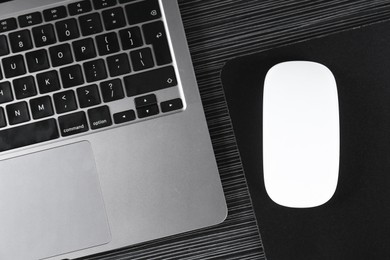 Photo of White computer mouse with mousepad and laptop on black wooden table, flat lay