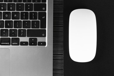 Photo of White computer mouse with mousepad and laptop on black wooden table, flat lay