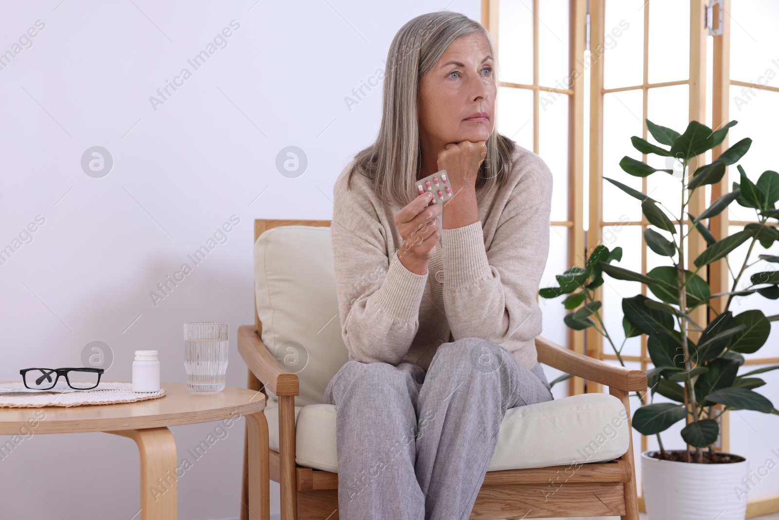 Photo of Senior woman holding blister with pills in armchair at home