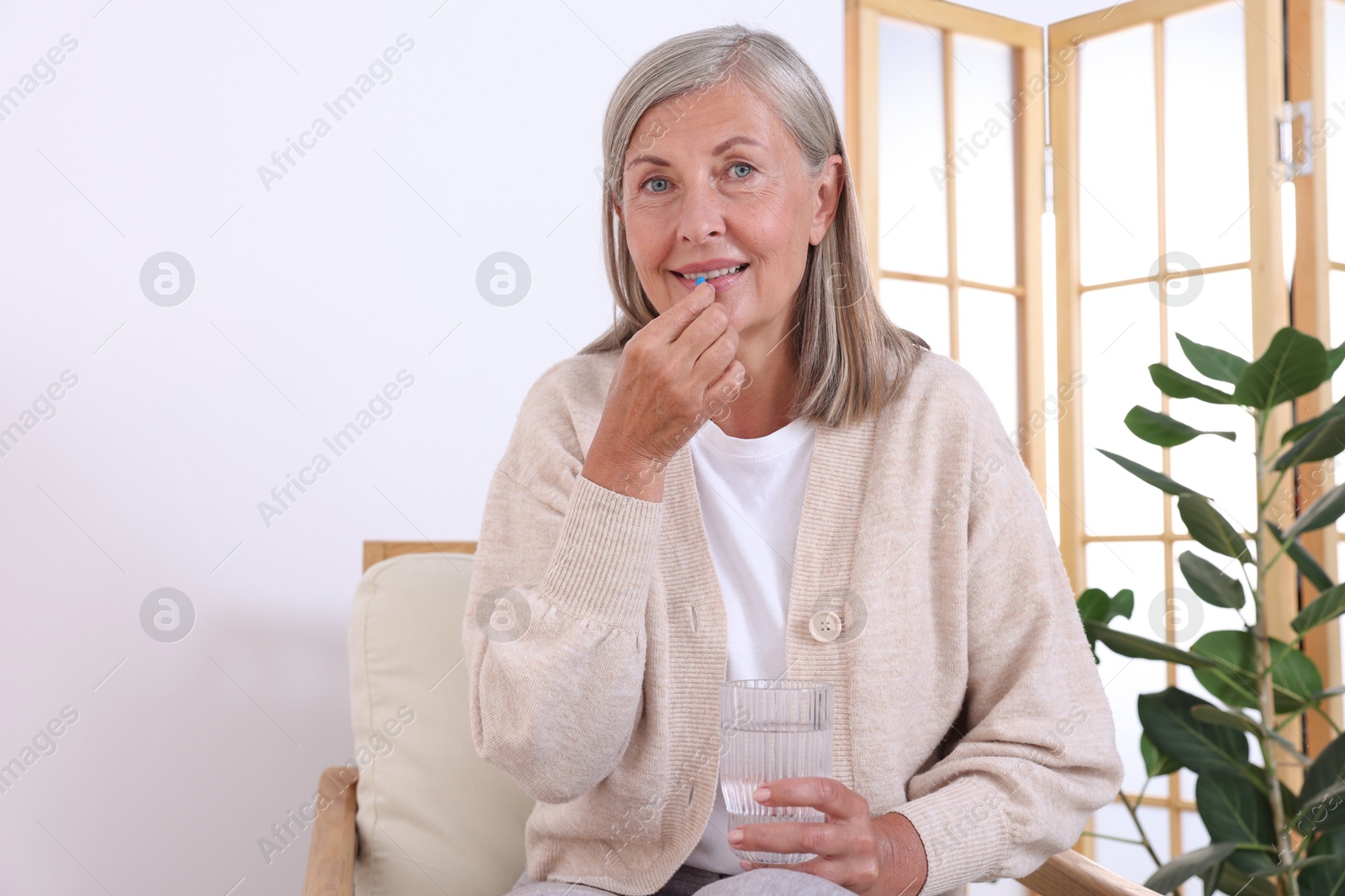 Photo of Senior woman with glass of water taking pill at home