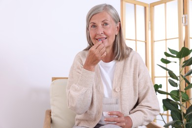 Photo of Senior woman with glass of water taking pill at home