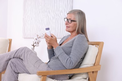 Senior woman with bottle of pills in armchair at home