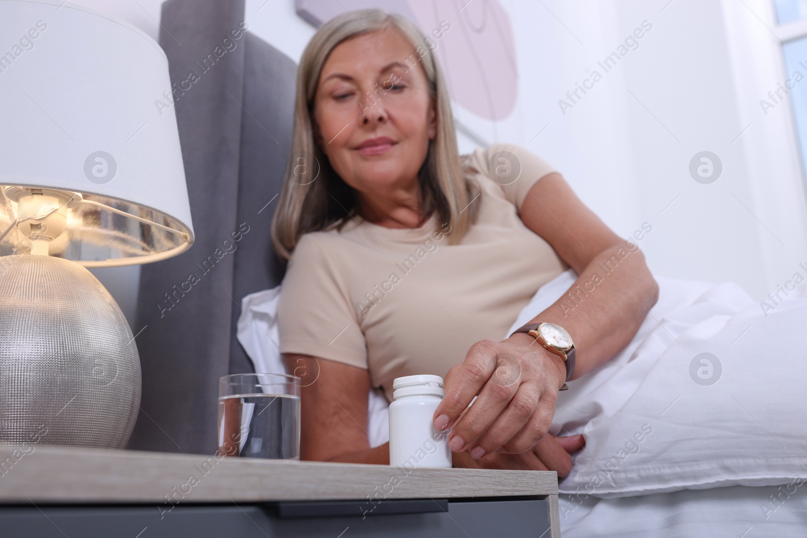 Photo of Senior woman taking pill bottle in bed at home, low angle view