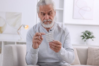 Photo of Senior man holding blister with pills at home