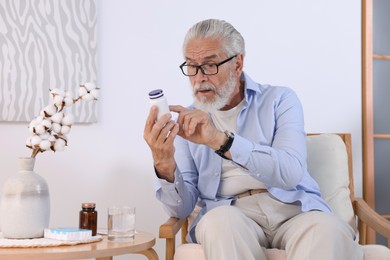 Senior man with bottle of pills at home