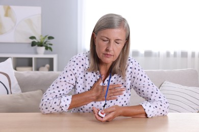 Photo of Senior woman suffering from heart pain pressing emergency call button at home