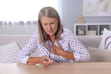 Photo of Senior woman suffering from heart pain pressing emergency call button at home