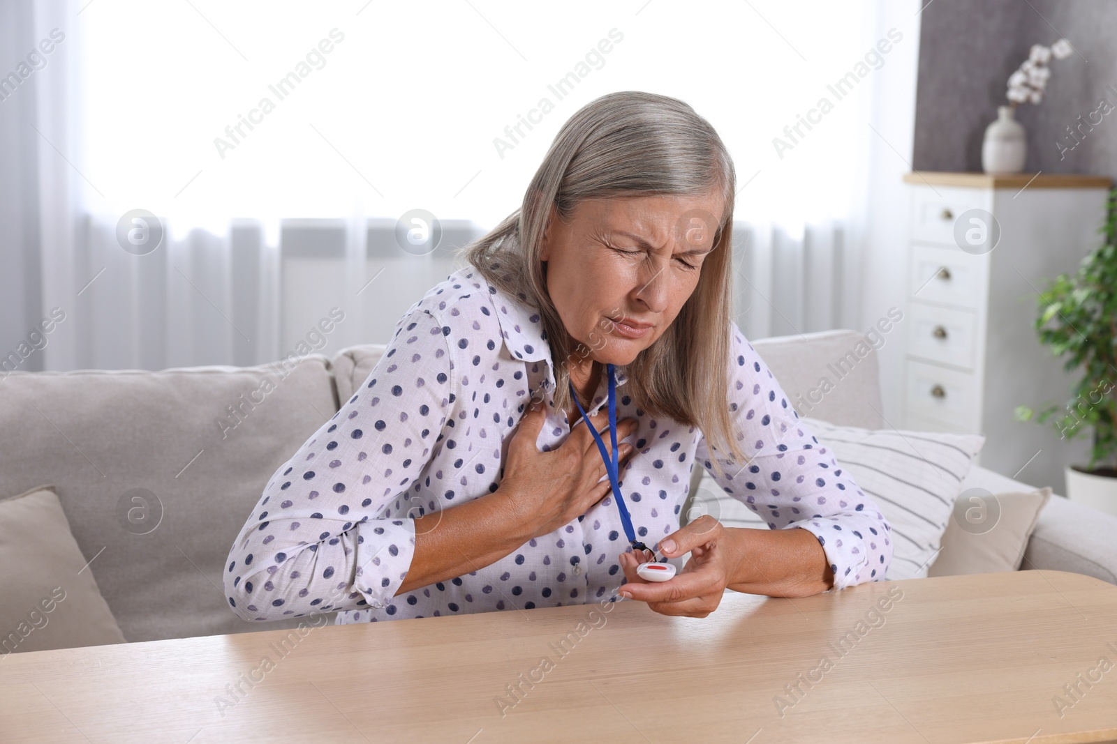 Photo of Senior woman suffering from heart pain pressing emergency call button at home