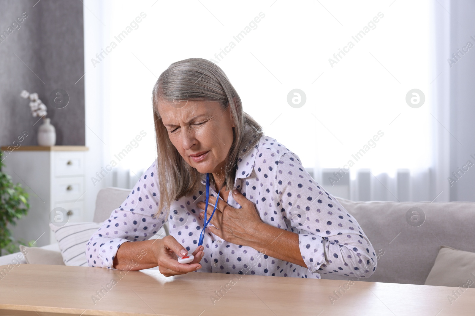 Photo of Senior woman suffering from heart pain pressing emergency call button at home