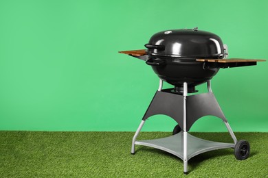 Photo of One black barbeque grill on grass against green background. Space for text