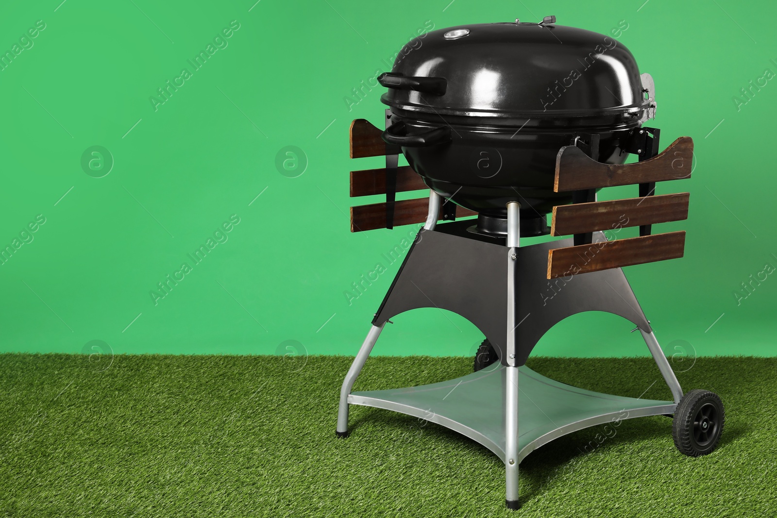 Photo of One black barbeque grill on grass against green background. Space for text