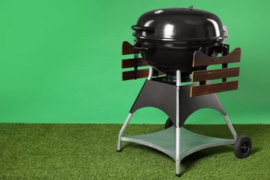 Photo of One black barbeque grill on grass against green background. Space for text