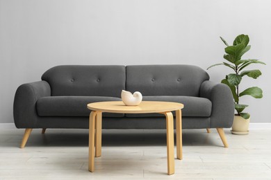 Photo of Comfortable sofa, houseplant and table near grey wall in room