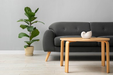 Photo of Comfortable sofa, houseplant and table near grey wall in room