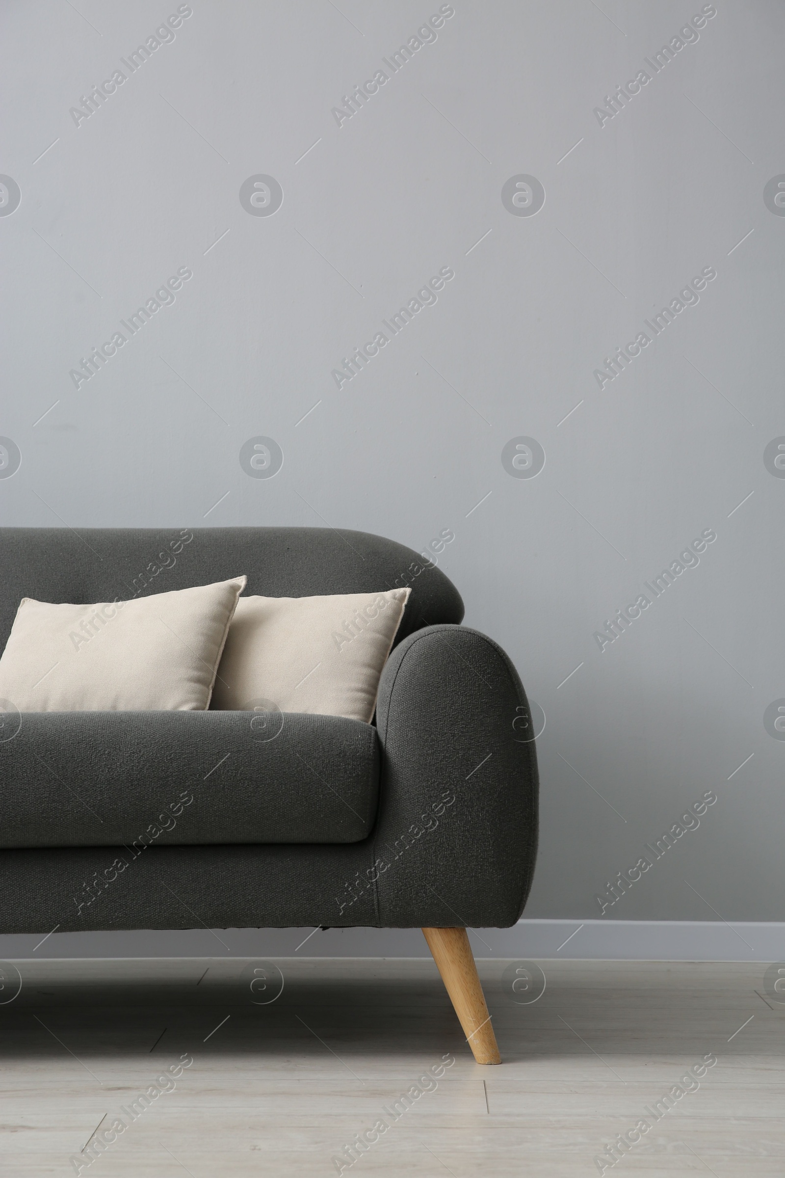 Photo of Comfortable sofa with cushions near grey wall in room, space for text