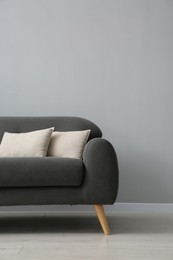 Comfortable sofa with cushions near grey wall in room, space for text