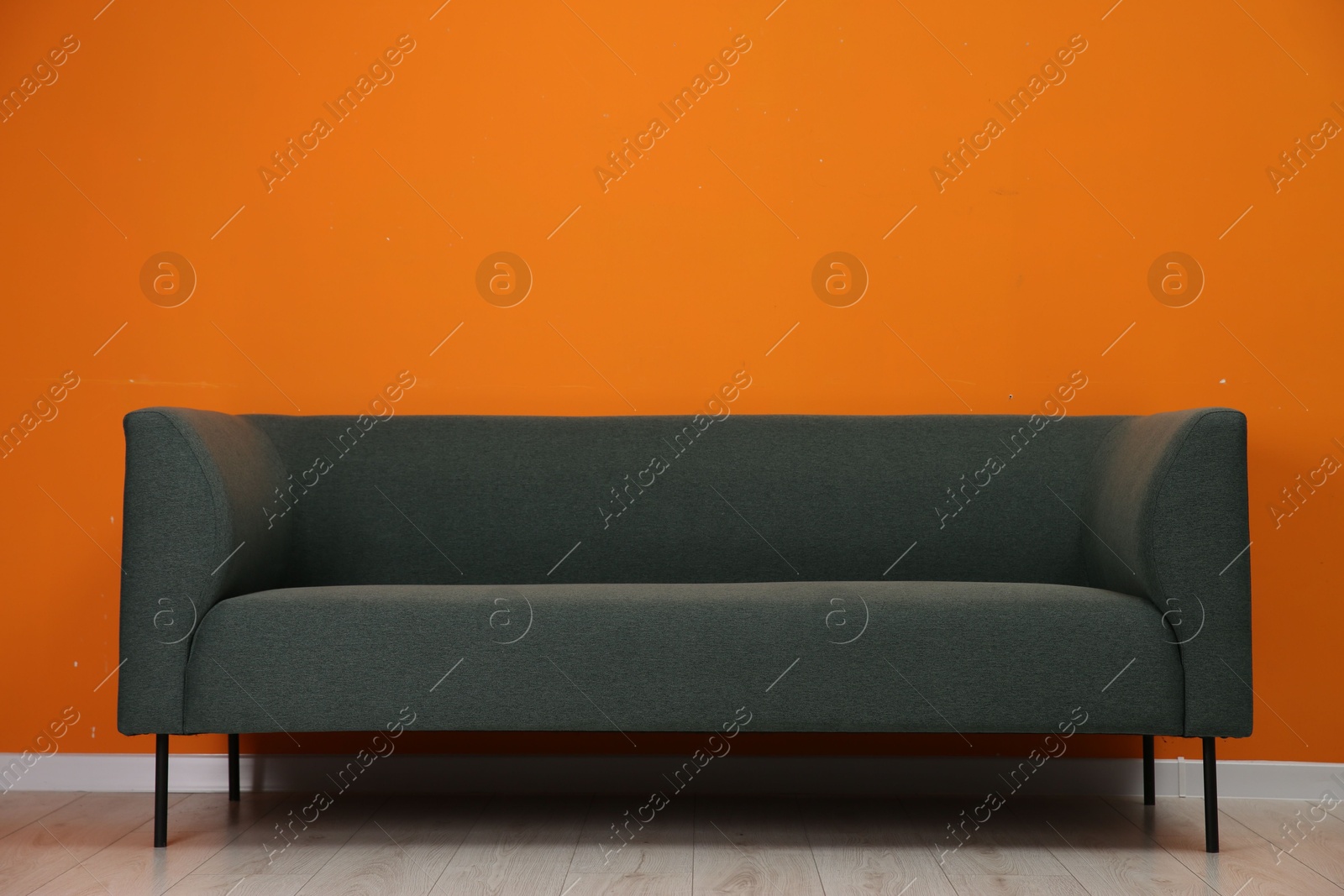 Photo of One stylish sofa near orange wall indoors