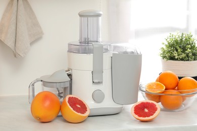 Photo of Modern juicer and grapefruits on white counter in kitchen