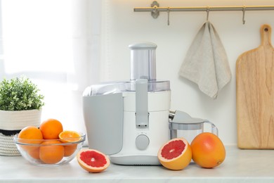 Photo of Modern juicer and grapefruits on white counter in kitchen