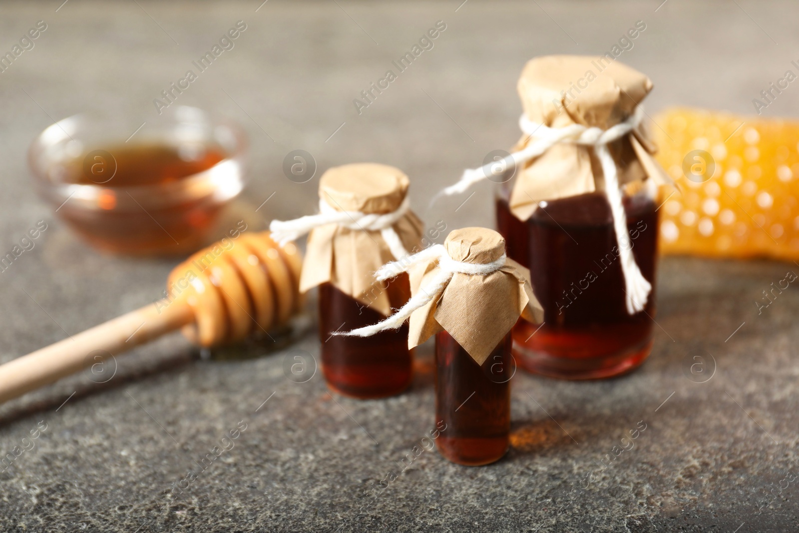 Photo of Honey tinctures, dipper and honeycomb on grey textured table, closeup. Alternative medicine