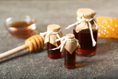 Photo of Honey tinctures, dipper and honeycomb on grey textured table, closeup. Alternative medicine