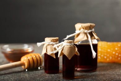 Photo of Honey tinctures, dipper and honeycomb on grey textured table, closeup. Alternative medicine