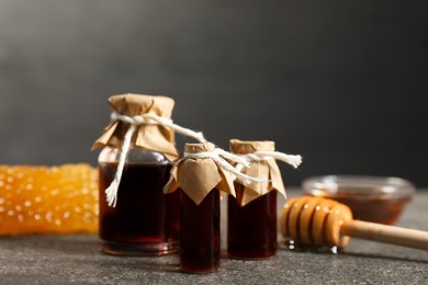 Photo of Honey tinctures, dipper and honeycomb on grey textured table, closeup. Alternative medicine