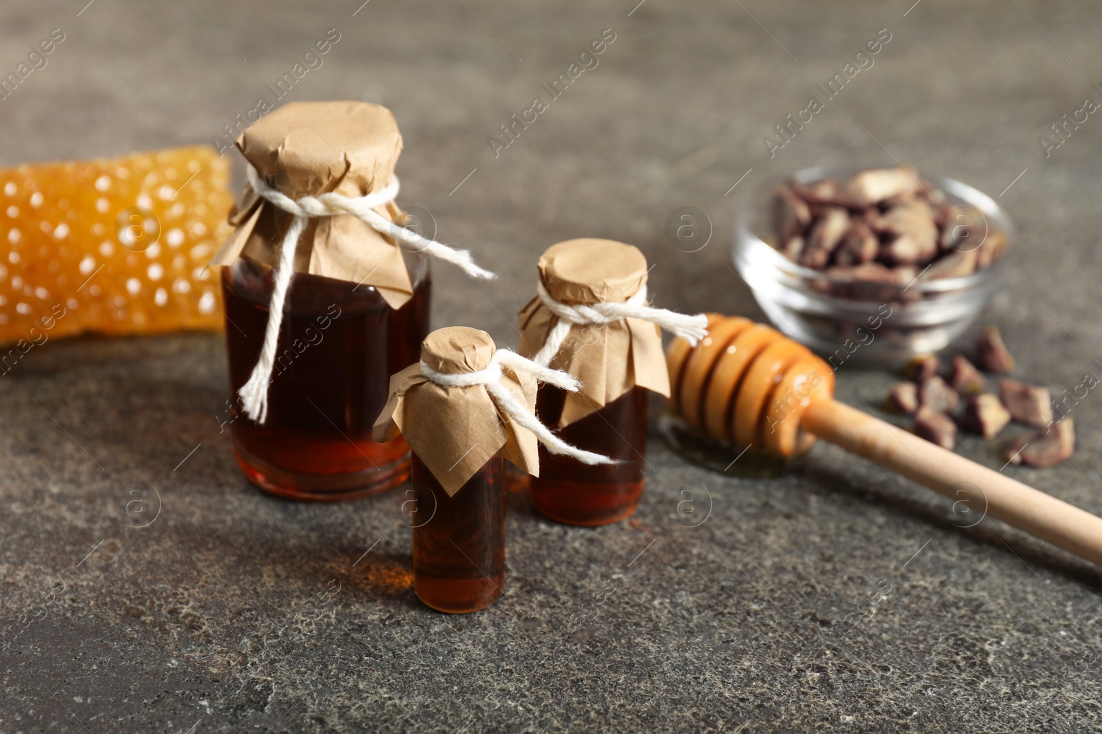 Photo of Honey tinctures, dipper and honeycomb on grey textured table, closeup. Alternative medicine