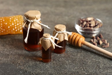 Photo of Honey tinctures, dipper and honeycomb on grey textured table, closeup. Alternative medicine