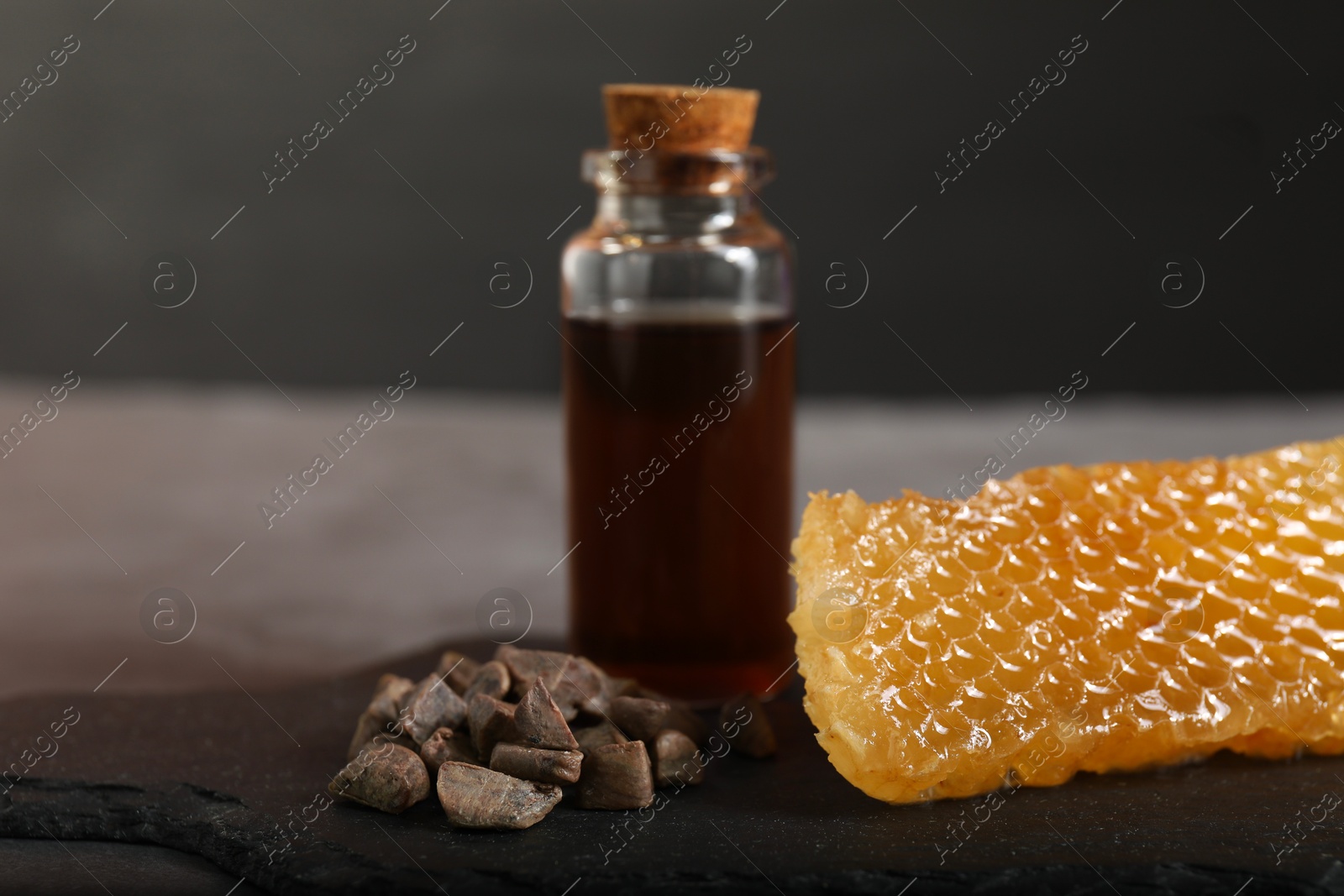 Photo of Honey tincture, honeycomb and pile of propolis granules on table, closeup. Alternative medicine