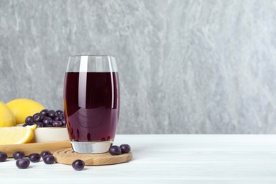 Photo of Tasty fresh acai juice in glass with berries and lemons on white wooden table, space for text