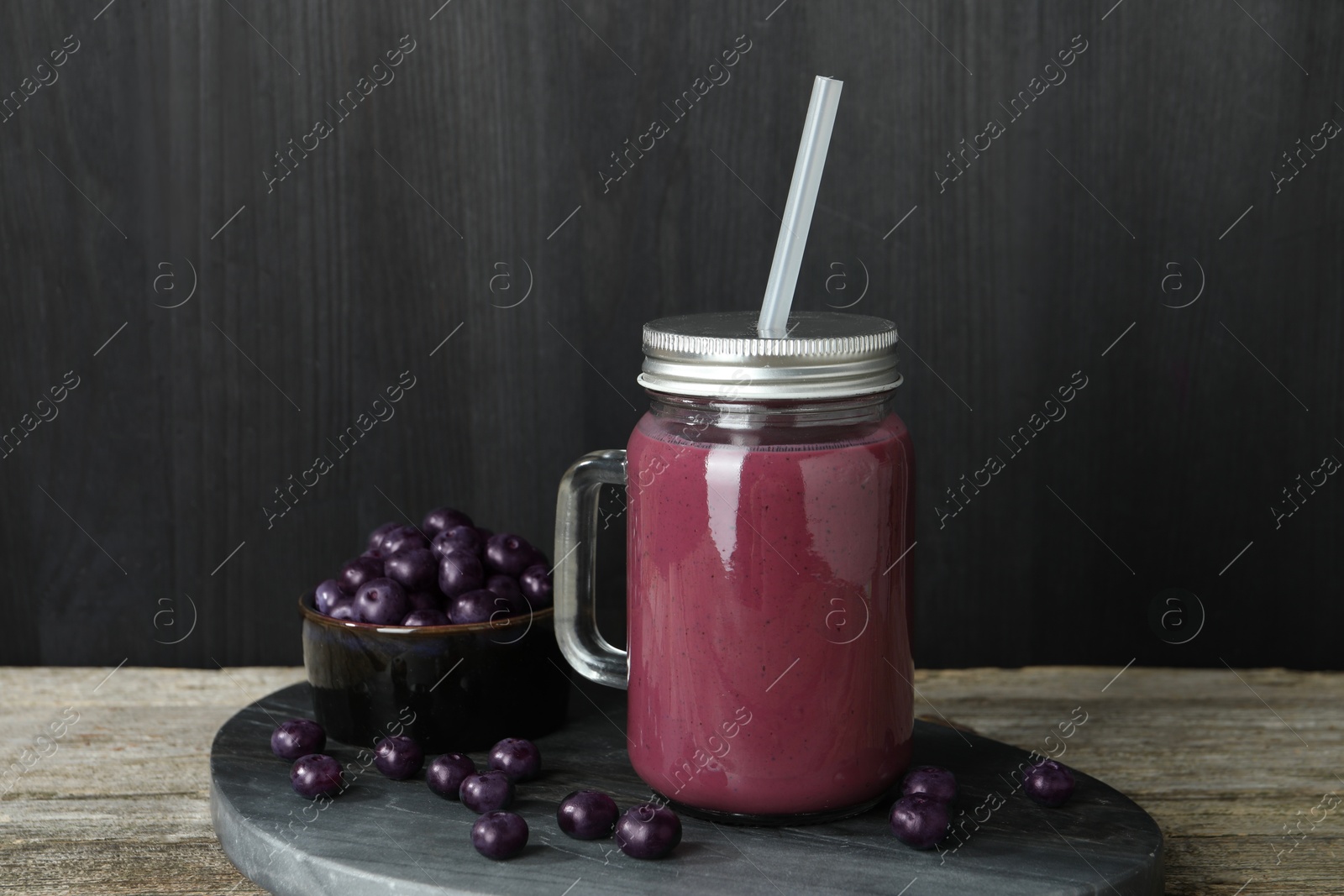 Photo of Tasty fresh acai juice in mason jar and berries on wooden table