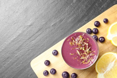 Photo of Tasty fresh acai juice in glass with berries and lemon on grey textured table, top view. Space for text