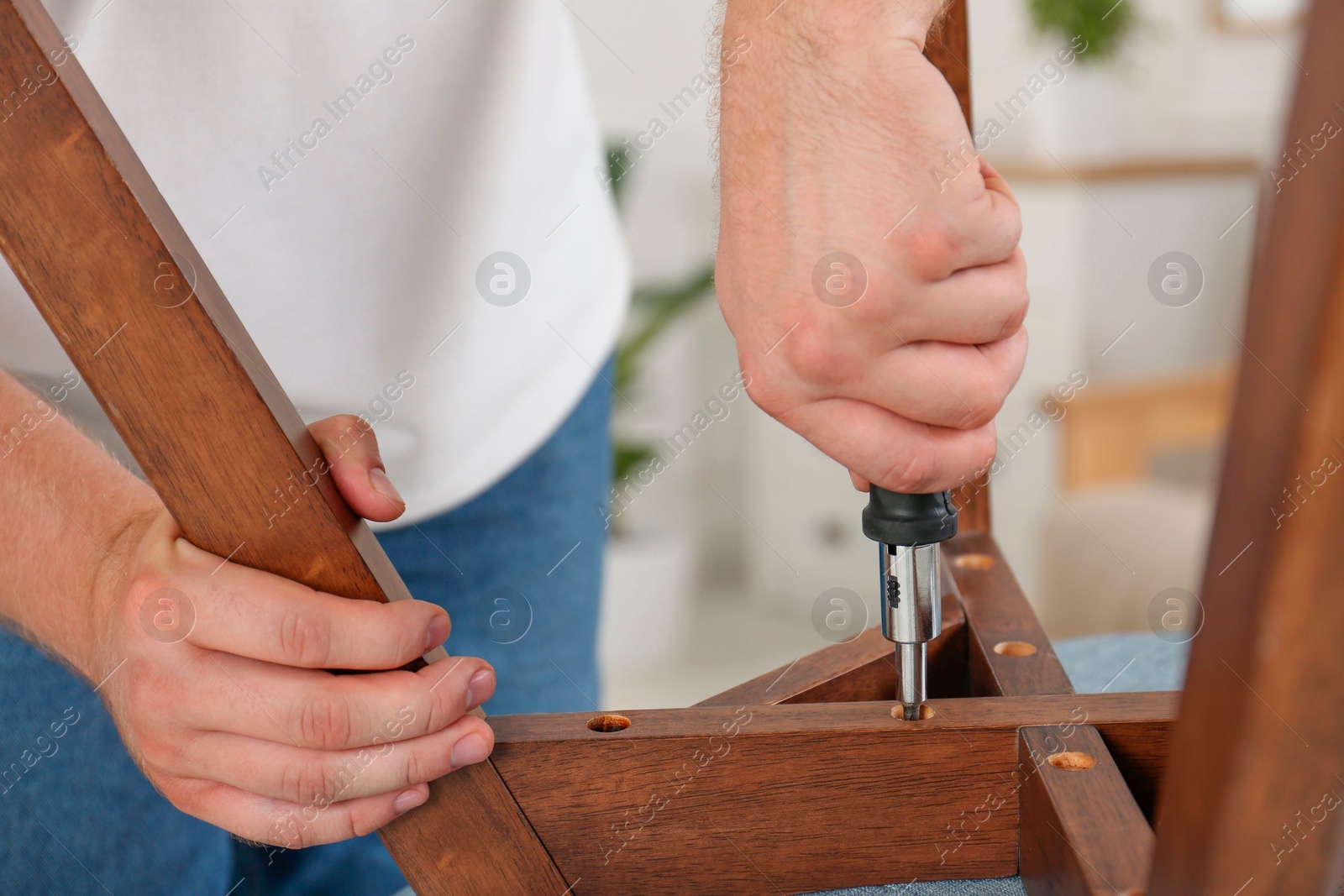 Photo of Man with screwdriver assembling furniture indoors, closeup