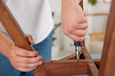 Man with screwdriver assembling furniture indoors, closeup