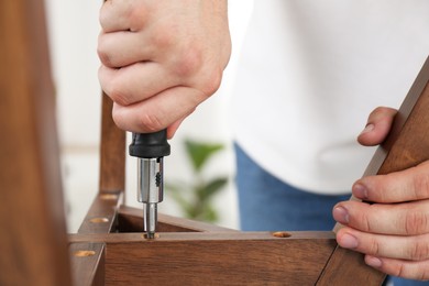 Photo of Man with screwdriver assembling furniture indoors, closeup