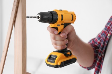 Man with electric screwdriver assembling furniture on white background, closeup