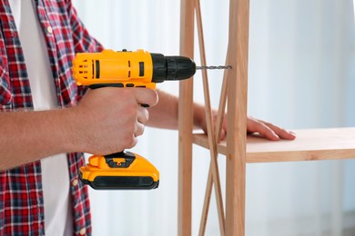 Photo of Man with electric screwdriver assembling furniture indoors, closeup