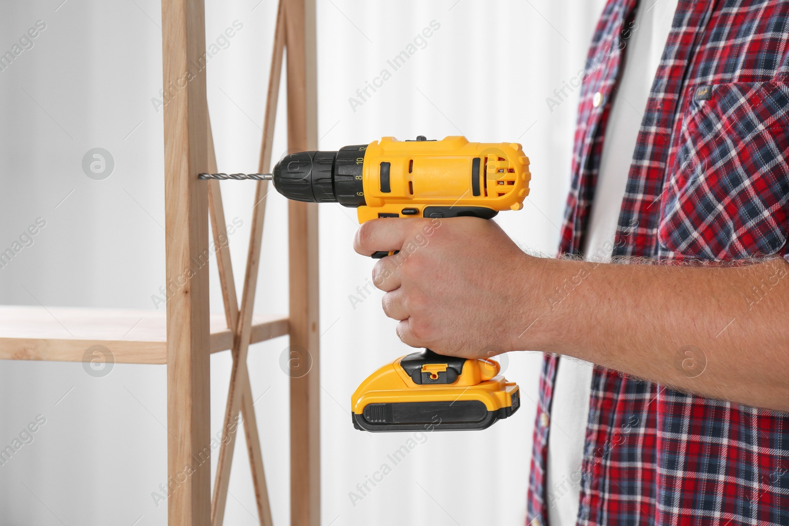 Photo of Man with electric screwdriver assembling furniture indoors, closeup