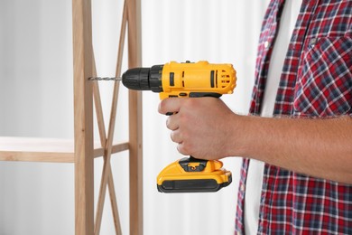 Photo of Man with electric screwdriver assembling furniture indoors, closeup