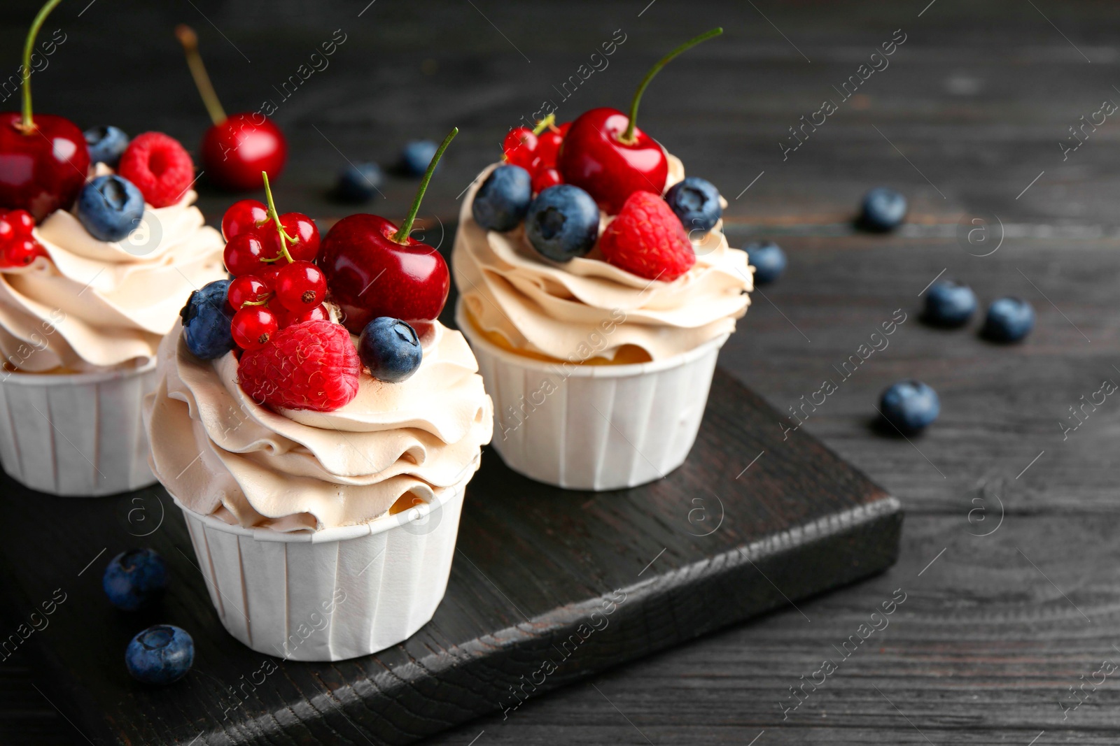 Photo of Tasty cupcakes with different berries on black wooden table, closeup