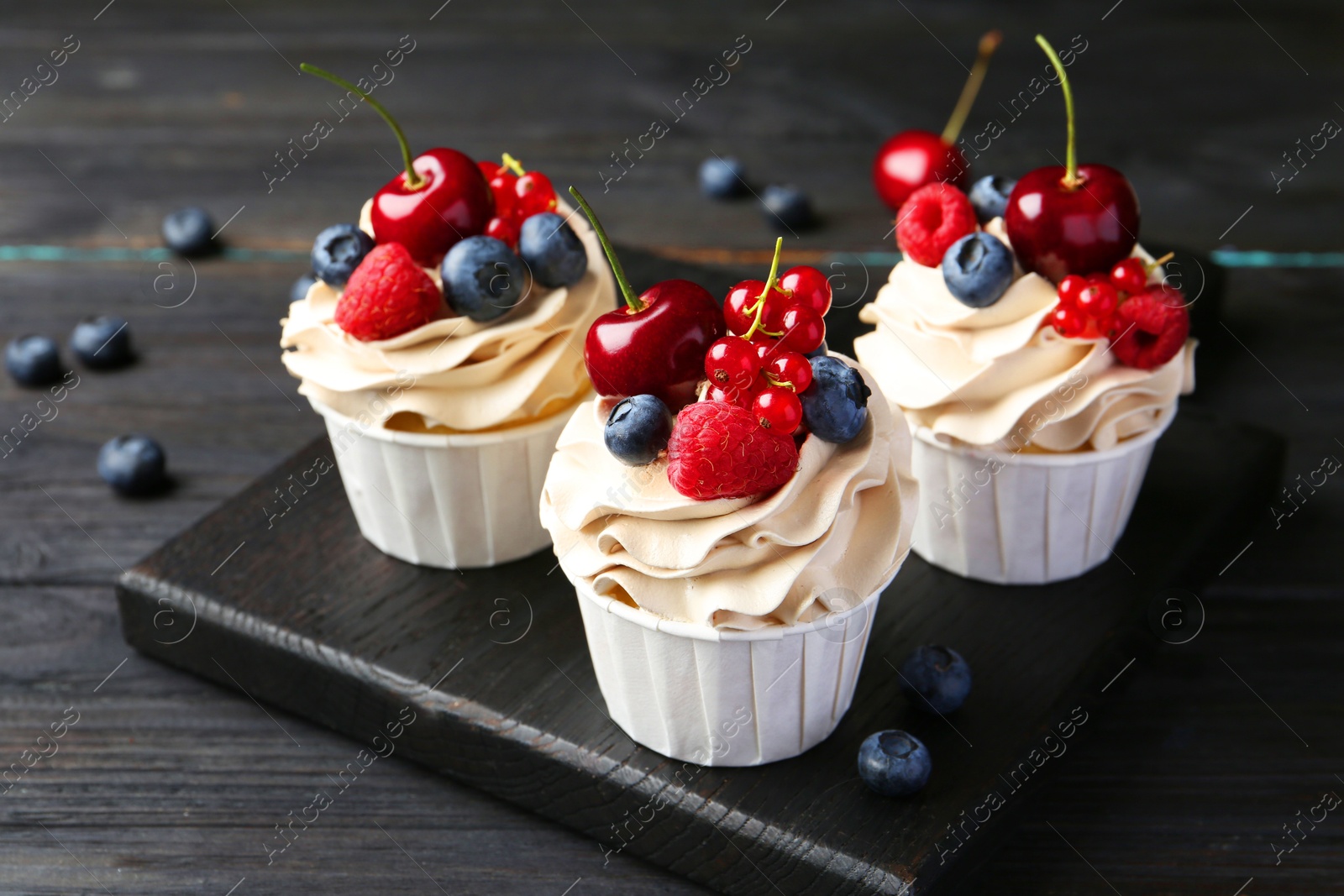 Photo of Tasty cupcakes with different berries on black wooden table, closeup